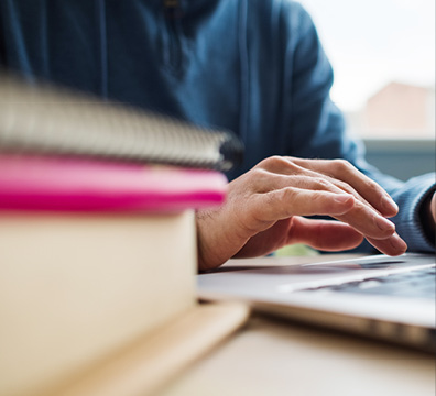 Man typing on laptop surrounded by books