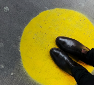 Person wearing black standing on a yellow dot on cement.  Image by Jon Tyson on Unsplash.