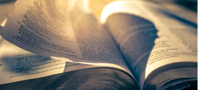Pages of a bible flipping in the wind with the sun backlighting the top of the book.  Image by Timothy Eberly on Unsplash.